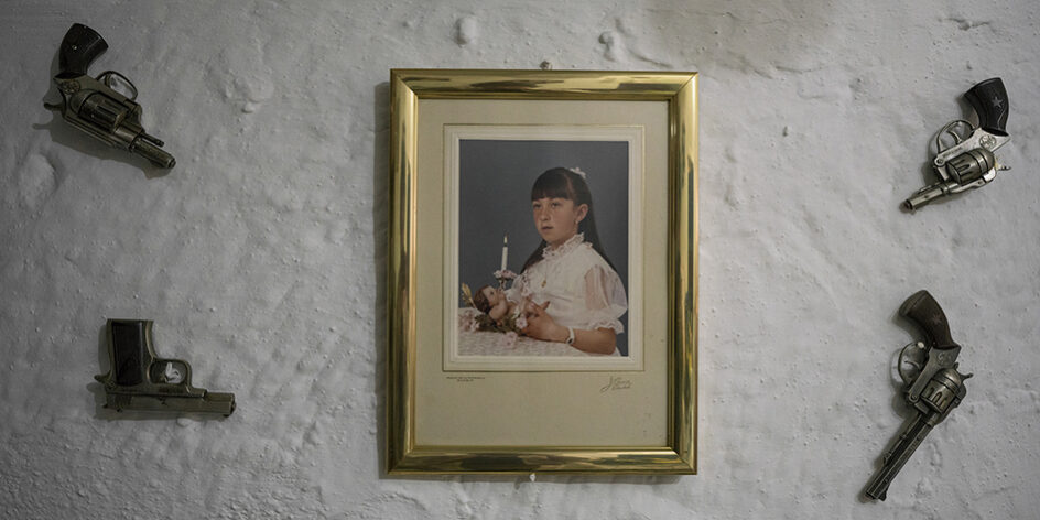 Tamara Merino, 2018 Decorazioni particolari sono comuni nelle caverne di Guadix. Qui, un residente ha appeso 4 pistole intorno a una foto di sua nipote, ritratta alla sua prima comunione. Andalusia, Spain.