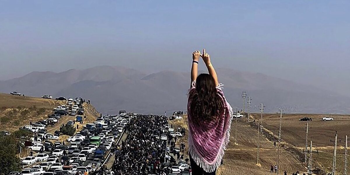 Marie Sumalla & Ghazal Golshiri, A young woman without a hijab stands on a vehicle as thousands of people make their way to the Aychi cemetery, to commemorate the 40th day of Mahsa Amini’s death, in Saqqez, her hometown in Iranian Kurdistan. Muslim tradition celebrates this date as the day of the soul’s passage to the afterlife, and the end of mourning, Saggez, Iranian Kurdistan, October 26, 2022, © Anonymous Author